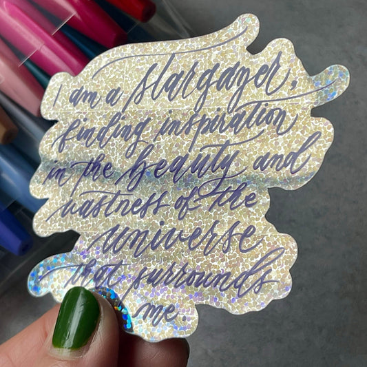 I am a stargazer finding inspiration in the beauty and vastness of the universe that surrounds me script calligraphy glitter sticker in shiny view.