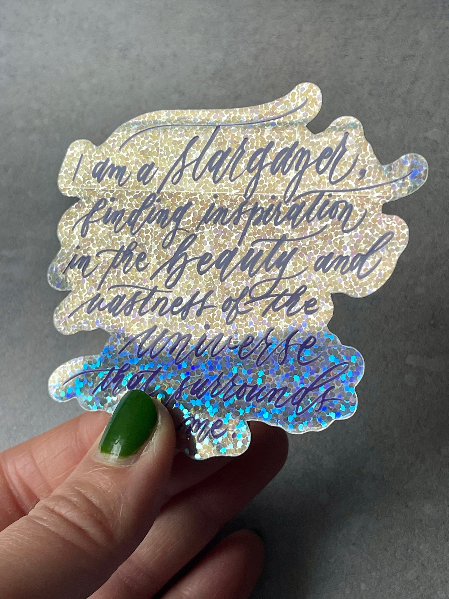 I am a stargazer finding inspiration in the beauty and vastness of the universe that surrounds me script calligraphy glitter sticker in shiny view to the side with blue ombre glitter at the bottom catching light.