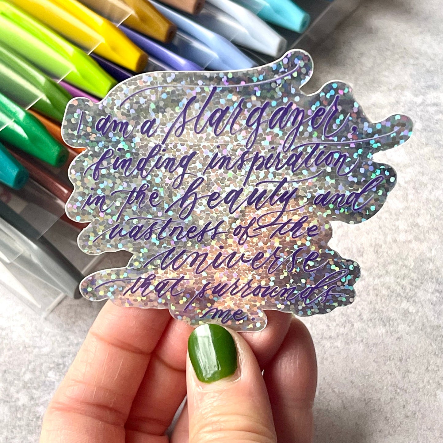 I am a stargazer finding inspiration in the beauty and vastness of the universe that surrounds me script calligraphy glitter sticker in shiny frontal view.