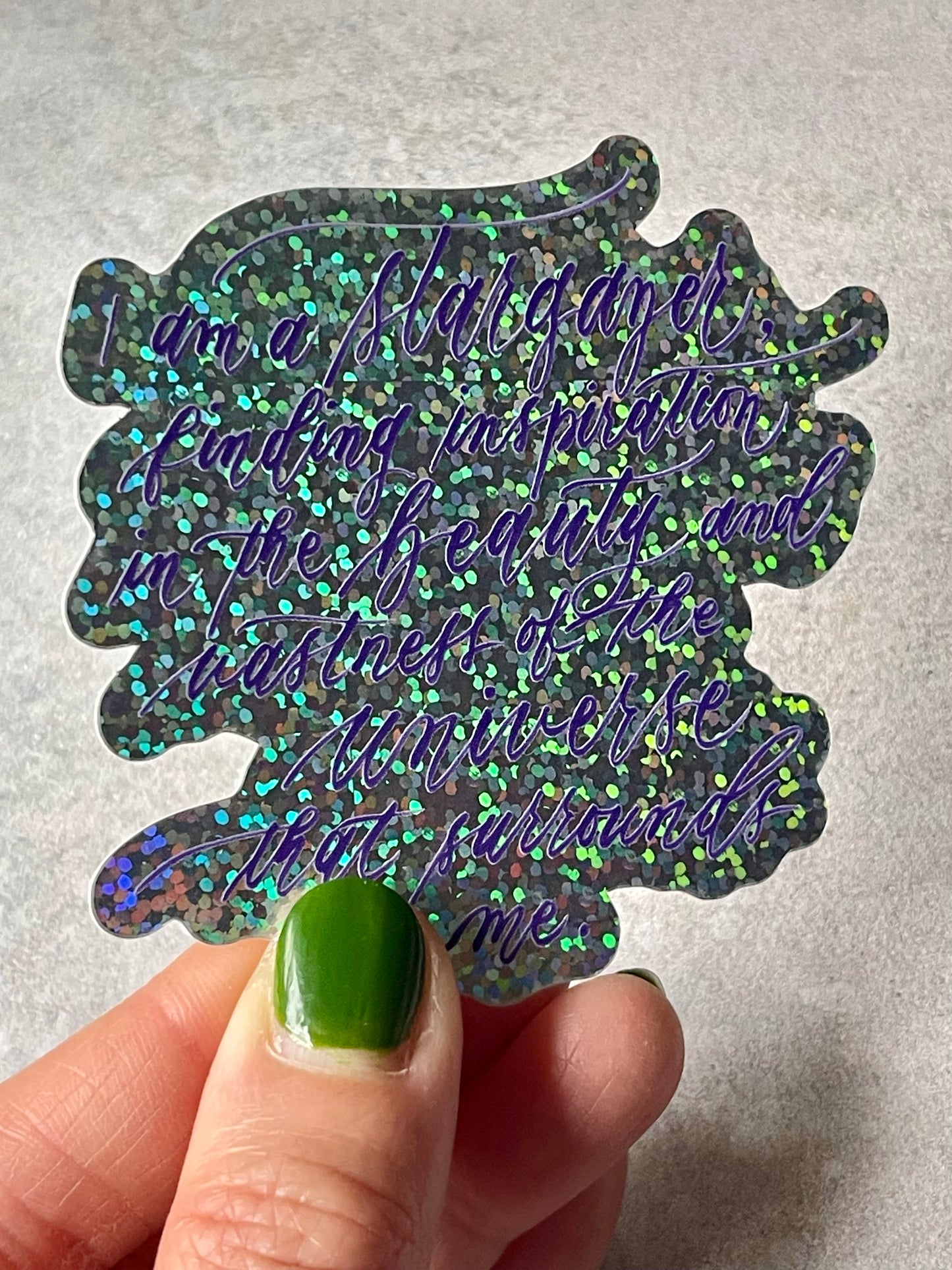 I am a stargazer finding inspiration in the beauty and vastness of the universe that surrounds me script calligraphy glitter sticker in glittery view and white lining to text.