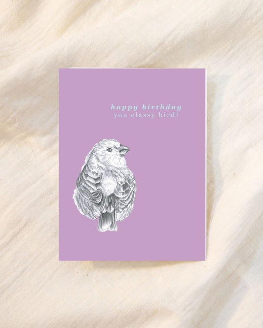 A square greeting card with a lavender purple background, featuring a white sketch of a bird and the text 'happy birthday you classy bird!' in light blue, displayed on a beige textured fabric background.