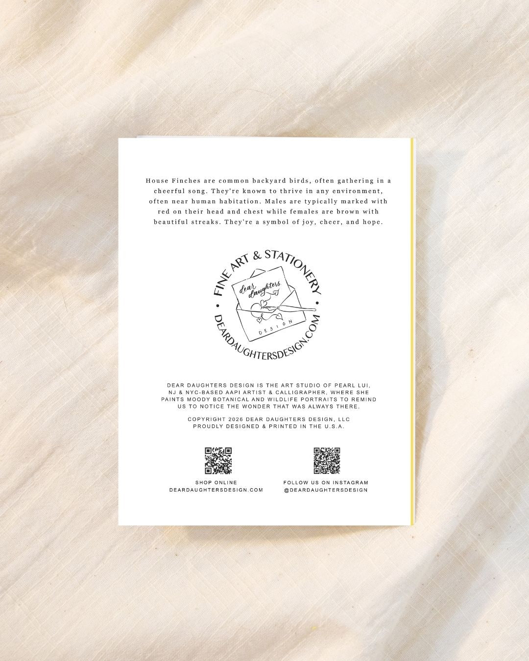 A white rectangular printed card with black text and a circular logo, photographed flat on a light beige marble-like surface. The card is a greeting card back for bird lovers and bird watchers, with visible text about House Finches and a circular stamp-style logo reading Fine Art & Stationery.