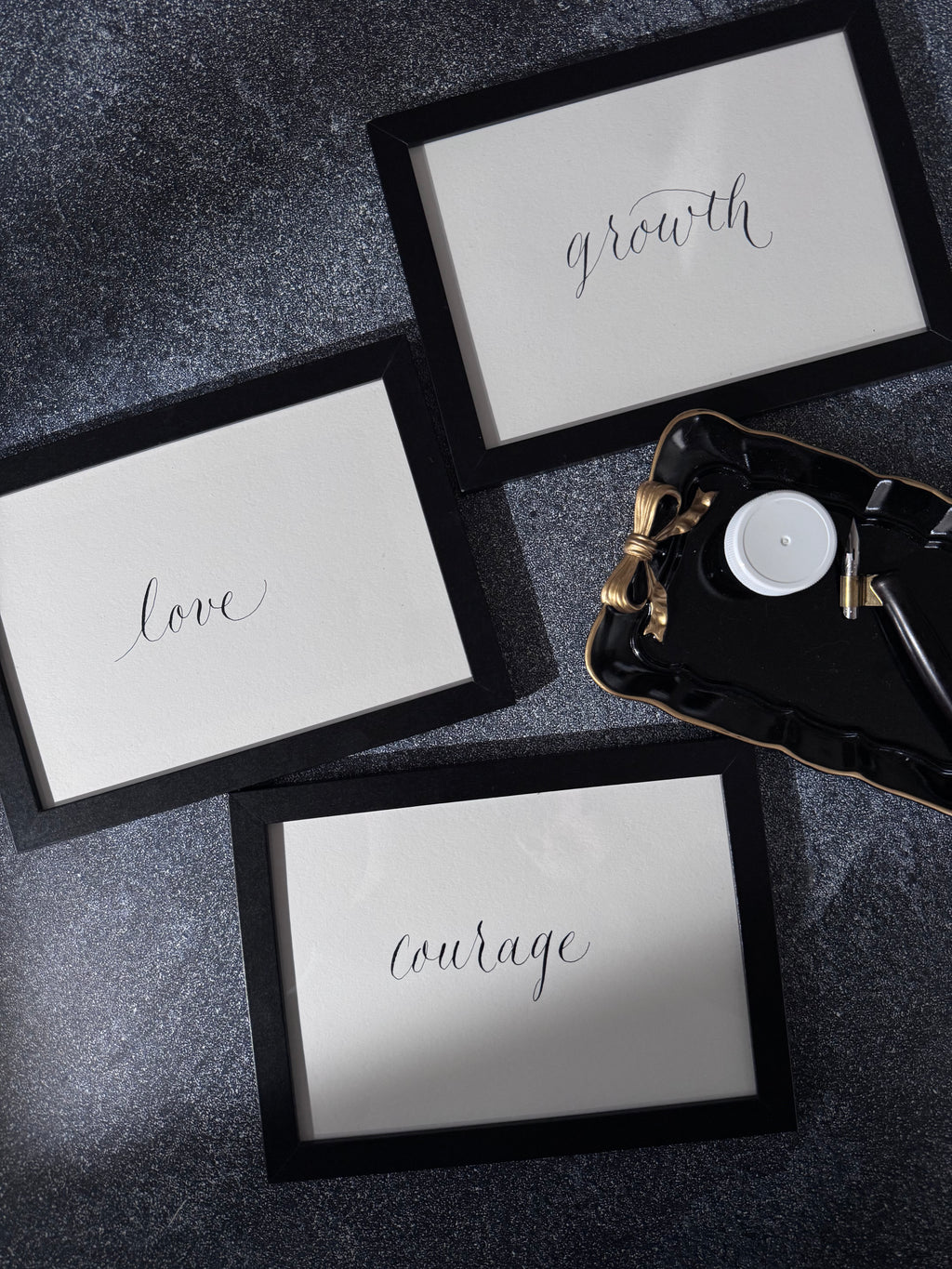 Three framed handwritten calligraphy with  motivational words on a dark textured surface.