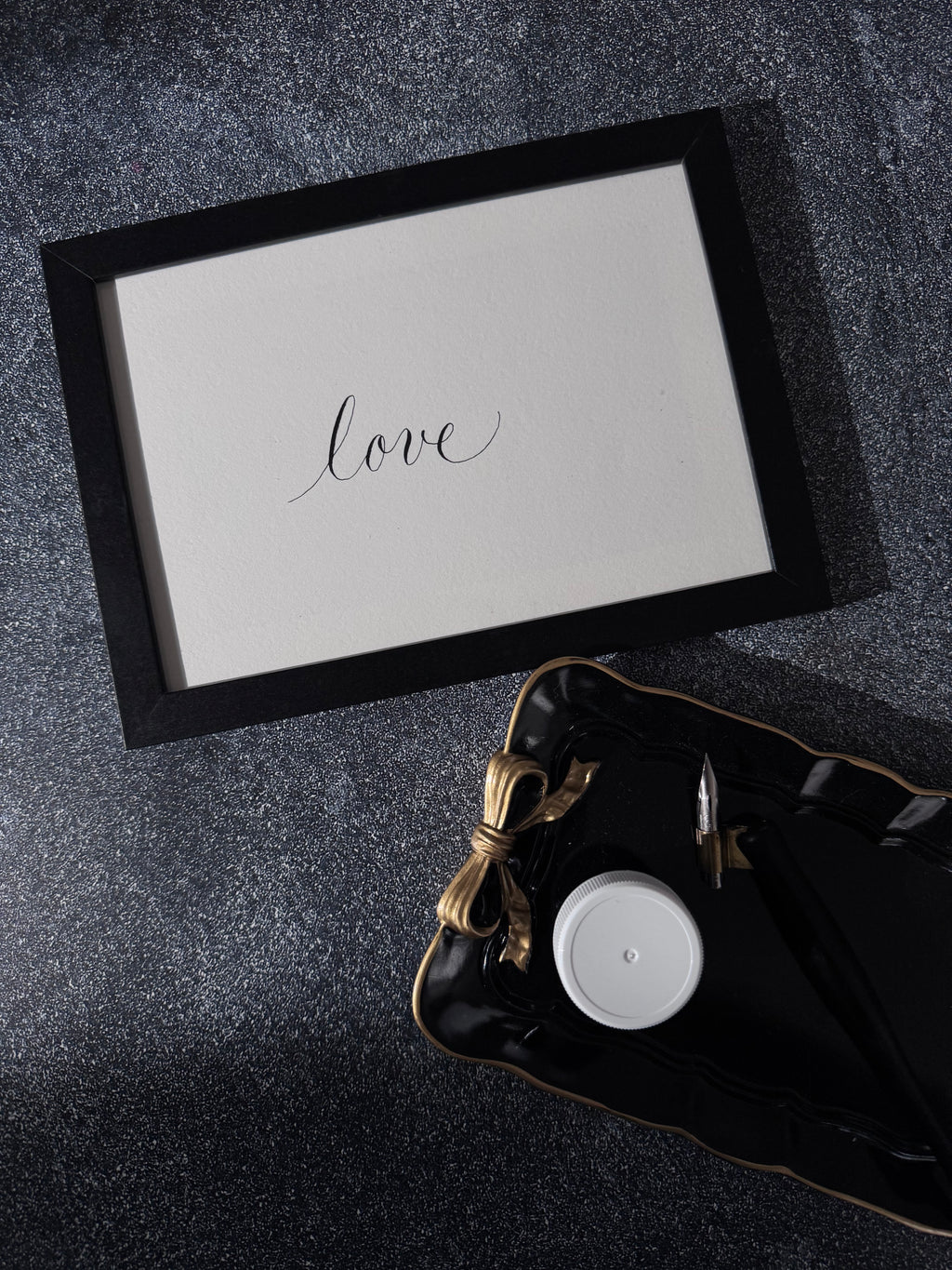 Pen nib on a piece of paper with 'love' written in calligraphy, against a textured black and white background by NJ Calligrapher.