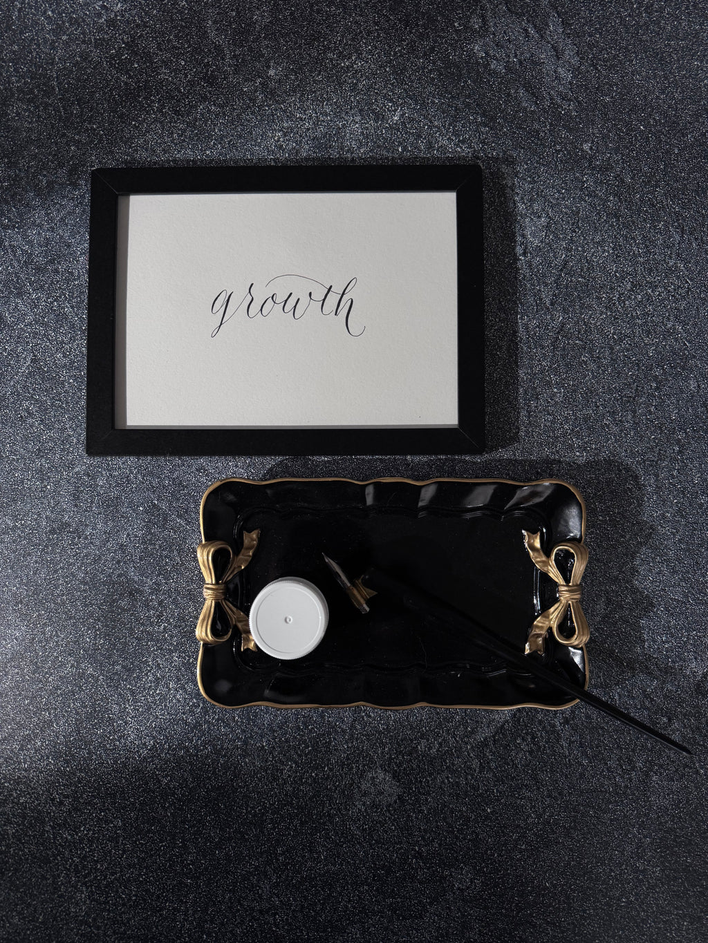 Decorative tray with ink jar and decorative items on a dark surface, framed artwork with 'growth' text by New Jersey calligrapher.