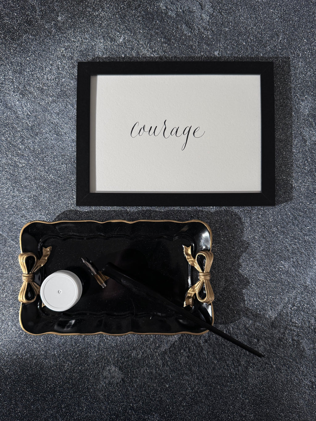 Black tray with decorative items on a dark surface, featuring a framed print with the word 'courage'.
