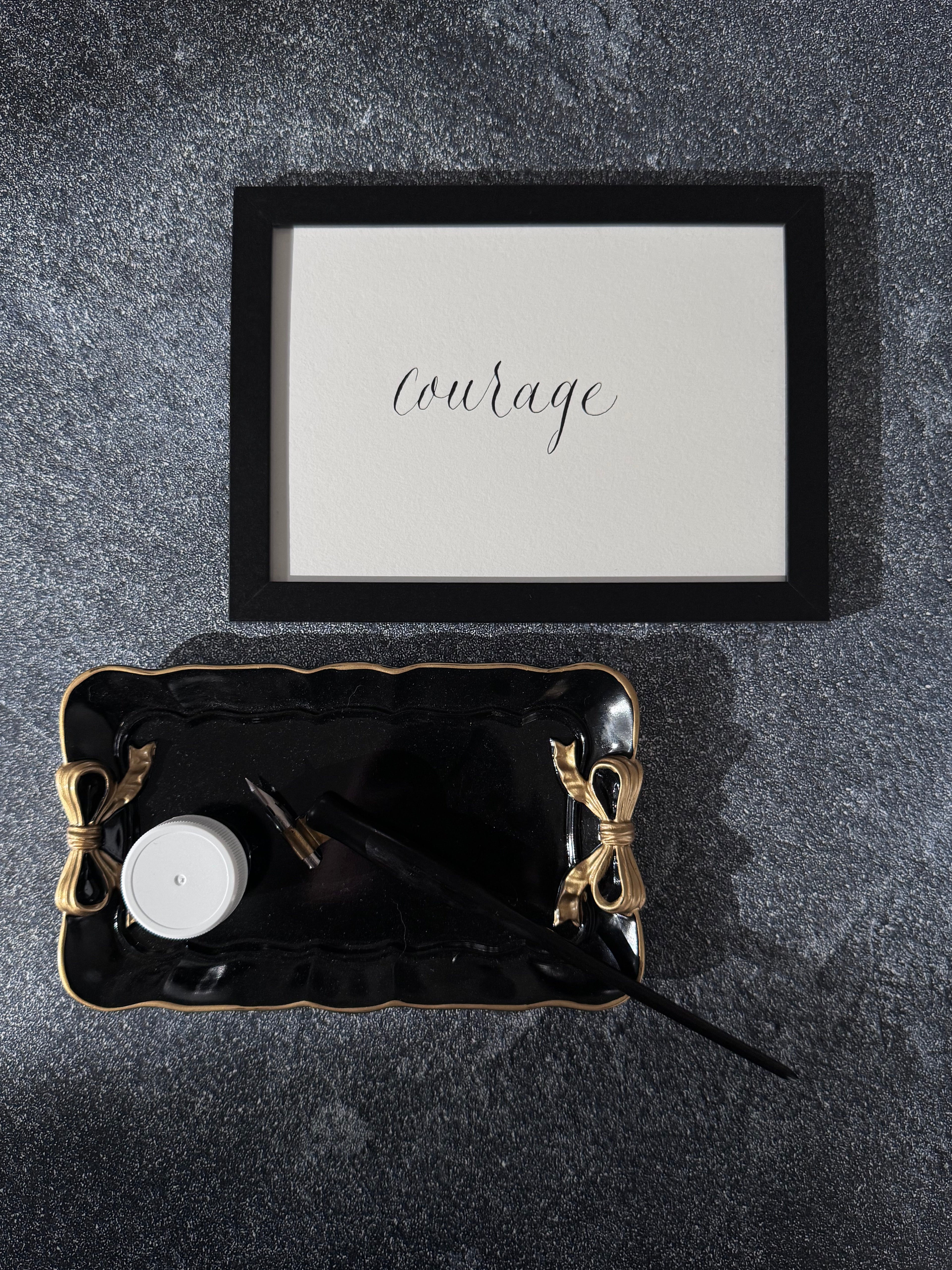 Black tray with decorative items on a dark surface, featuring a framed print with the word 'courage'.