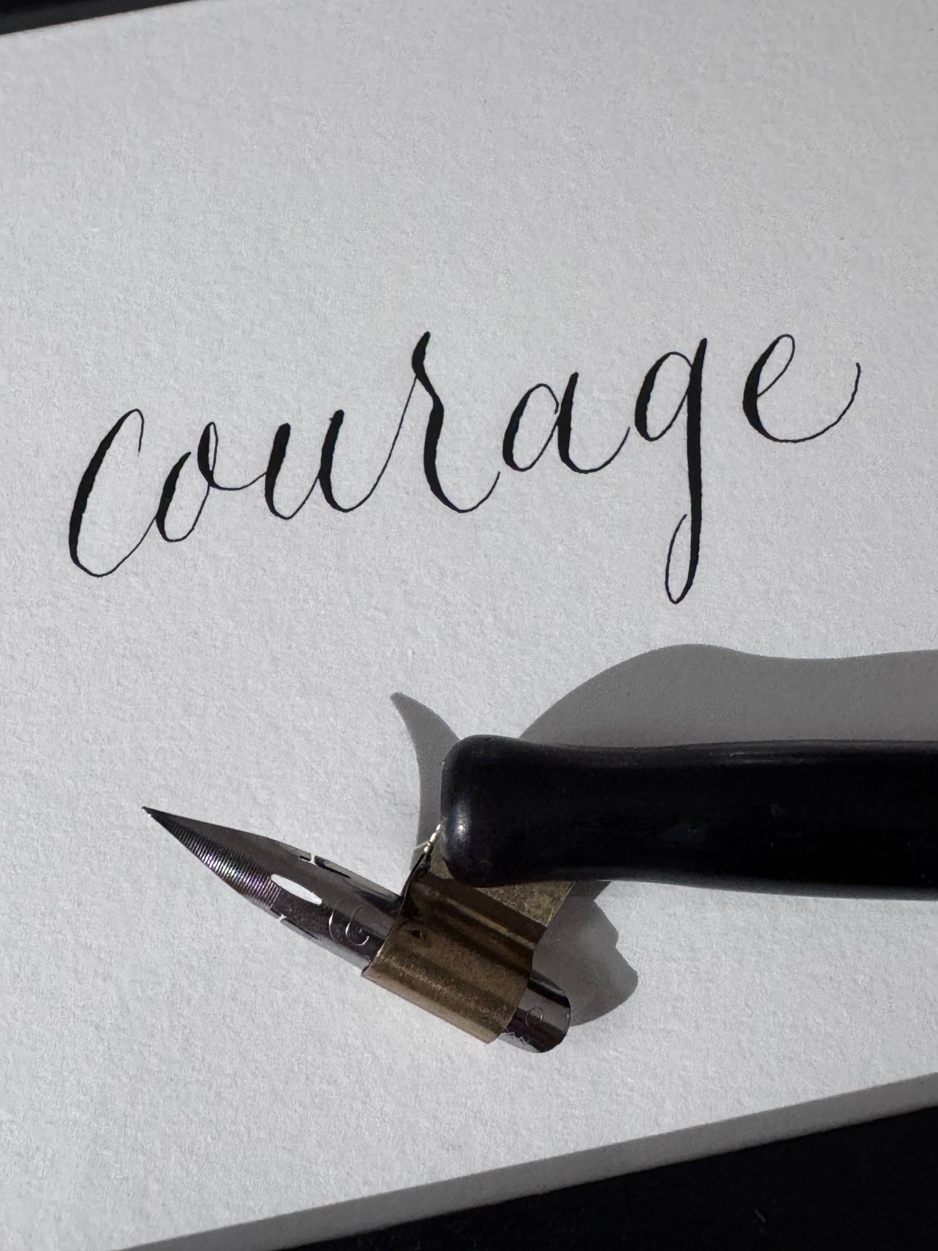 Calligraphy pen with ink stone on textured paper featuring the word 'Courage'.