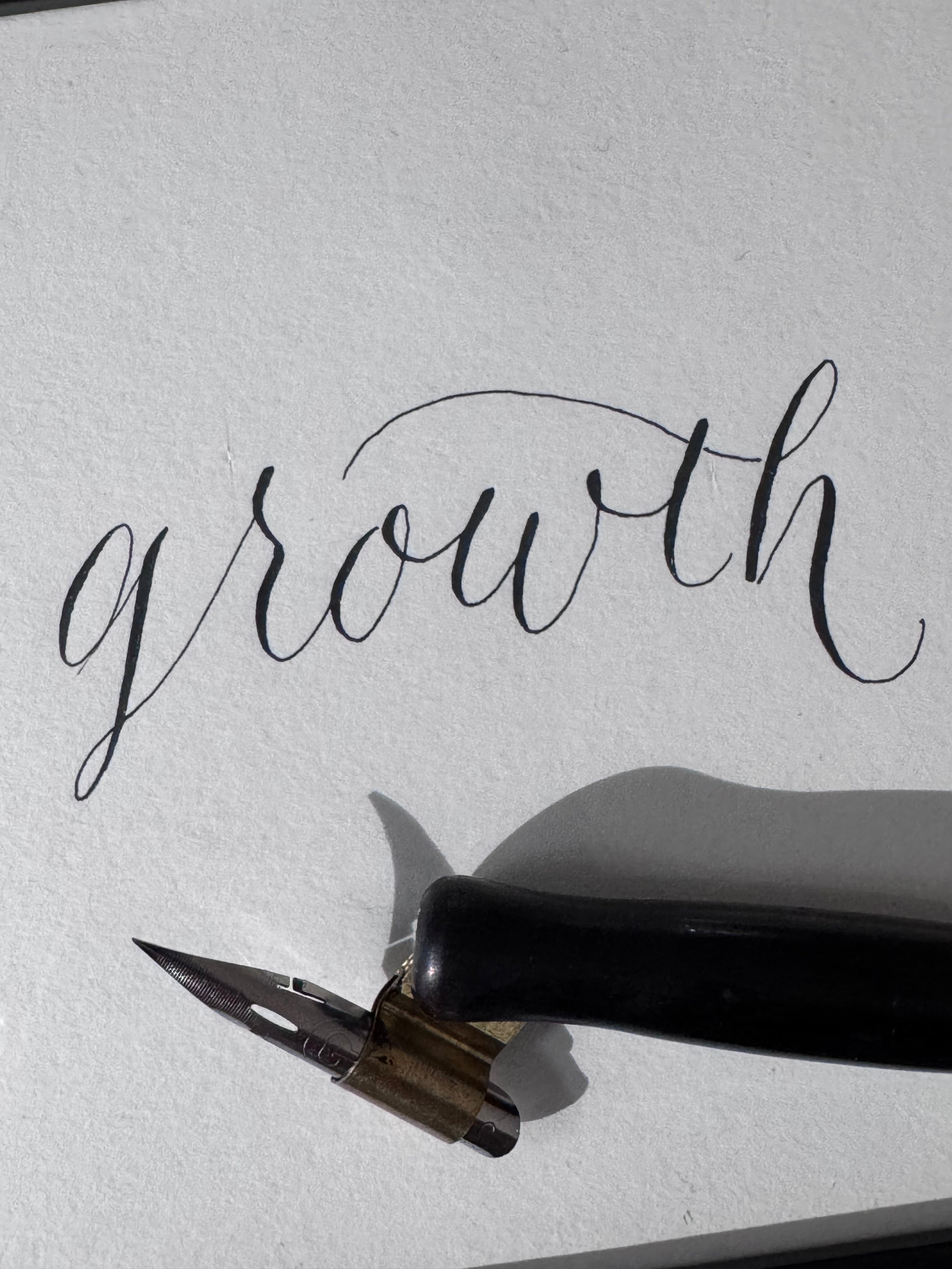 Calligraphy pen with ink bottle on paper displaying the word 'growth' by NJ calligrapher in Short Hills and Millburn, New Jersey.